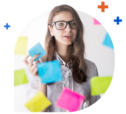 A woman holding a blue sticky note arranging colored sticky notes on a wall in front of her